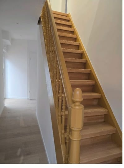 L'escalier terminé, vu depuis le bas : marches en bois clair, garde-corps tourné laqué, murs de la cage d'escalier repeints en blanc et parquet posé dans le couloir.